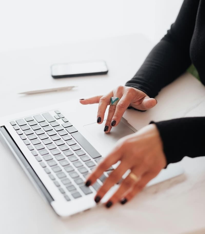 Web designer typing on laptop while planning SEO strategy for a Rochester MN business, pen, and a notebook on the desk. The person is wearing a ring on their left hand and black nail polish. Performing Expert Website optimization SEO services.